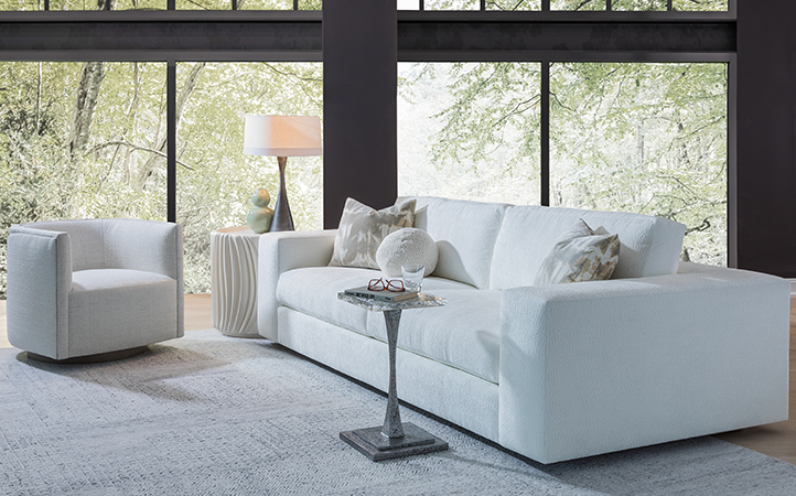 Artistica Upholstery scene featuring a white sofa and chair, a white side table and a pewter accent table with a clear top.