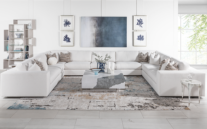 Artistica Upholstery scene featuring a white sectional, a white bookcase, a marble look side table and a white and gray cocktail table.